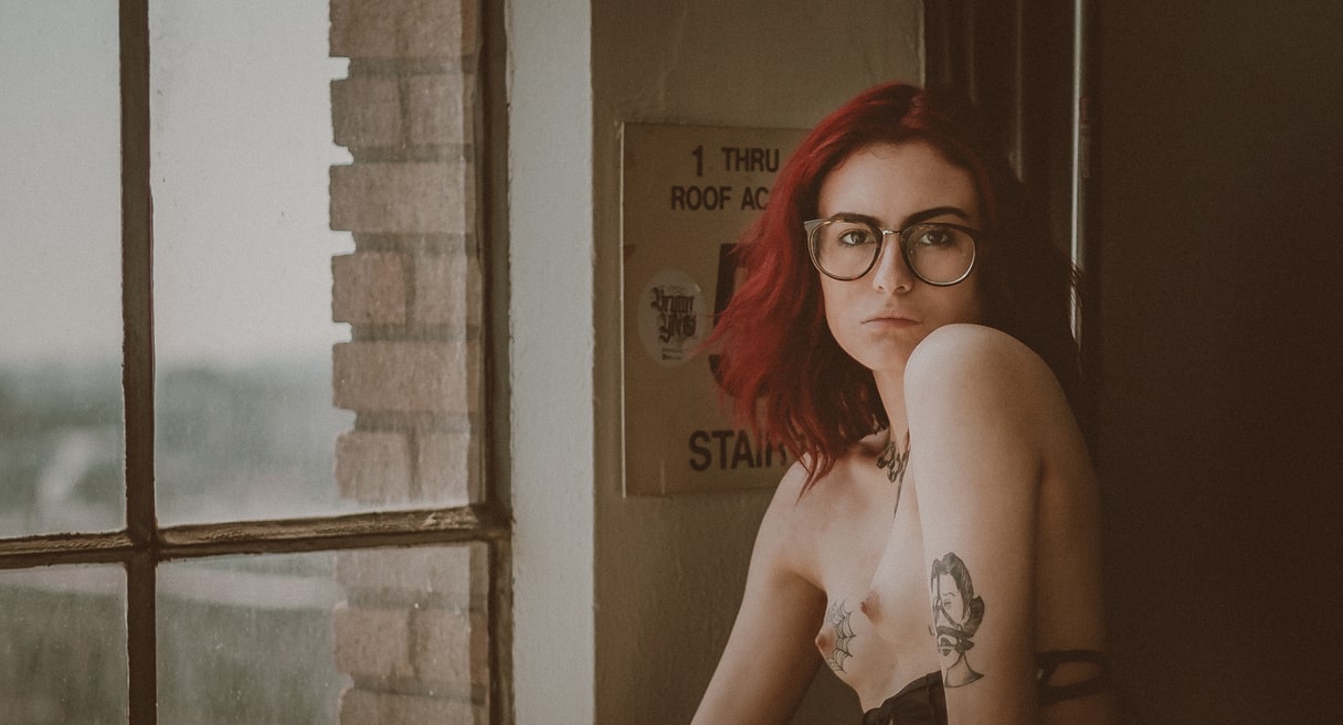 Portrait of a bespectacled topless woman standing by the window