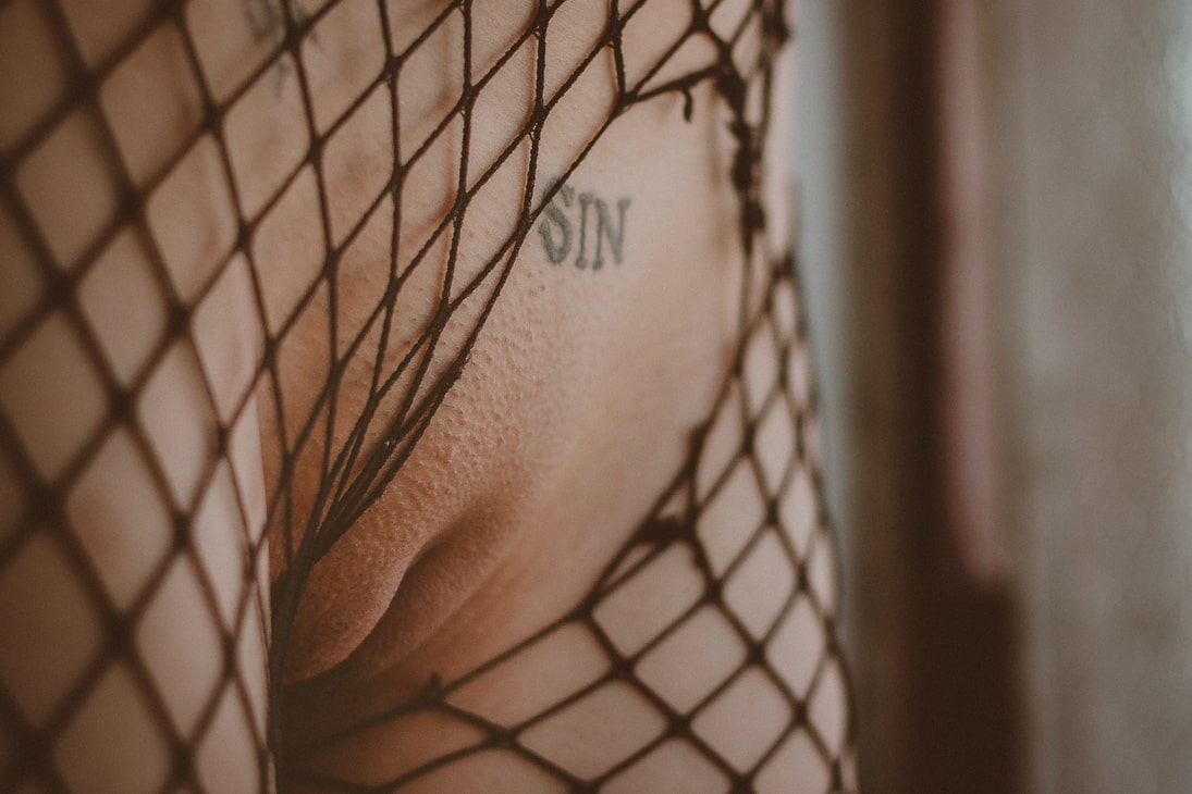 Detail of a woman's shaved vagina with the word 'sin' tattooed on her mound