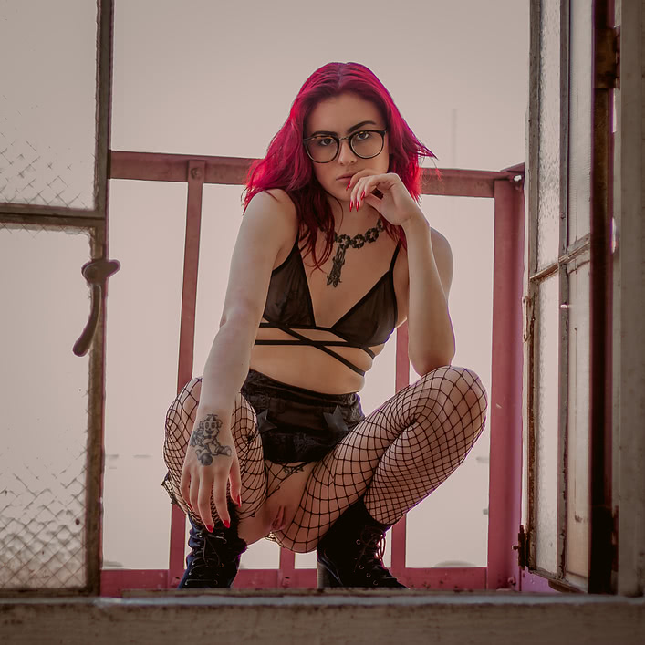 She squats on the fire escape revealing her shaved vagina through her crotchless fishnets