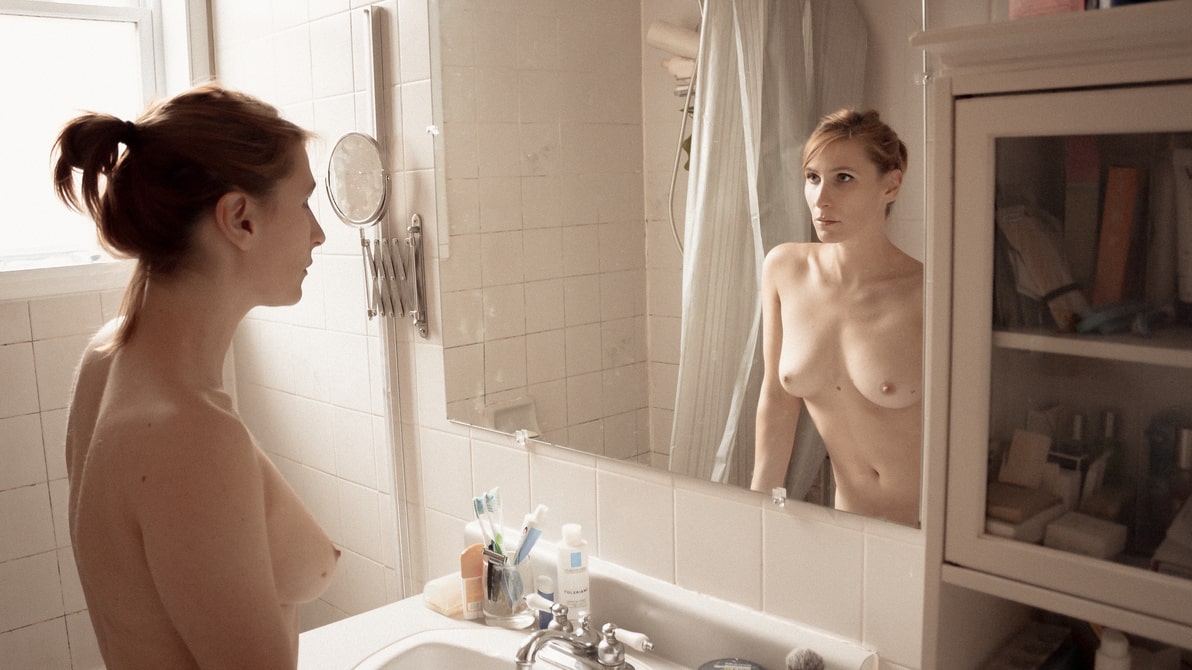 Topless woman standing in front of her bathroom mirror