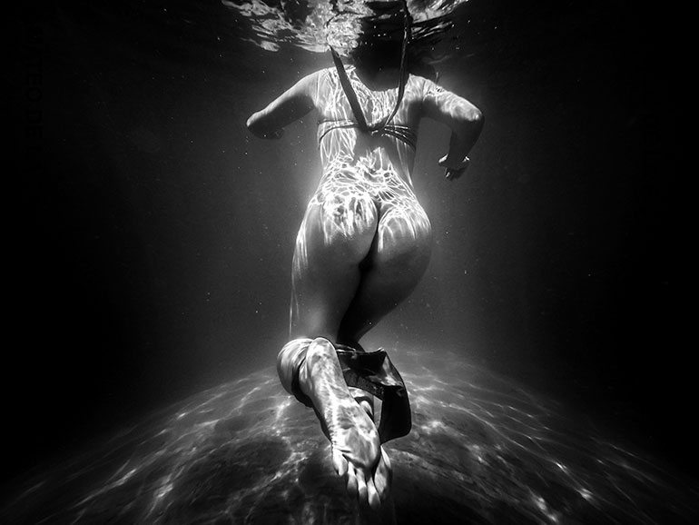 Underwater photo of a woman's nude backside as she removes her bikini bottoms
