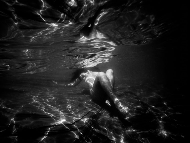 Underwater photo of nude woman crossing her legs and exposing her breasts