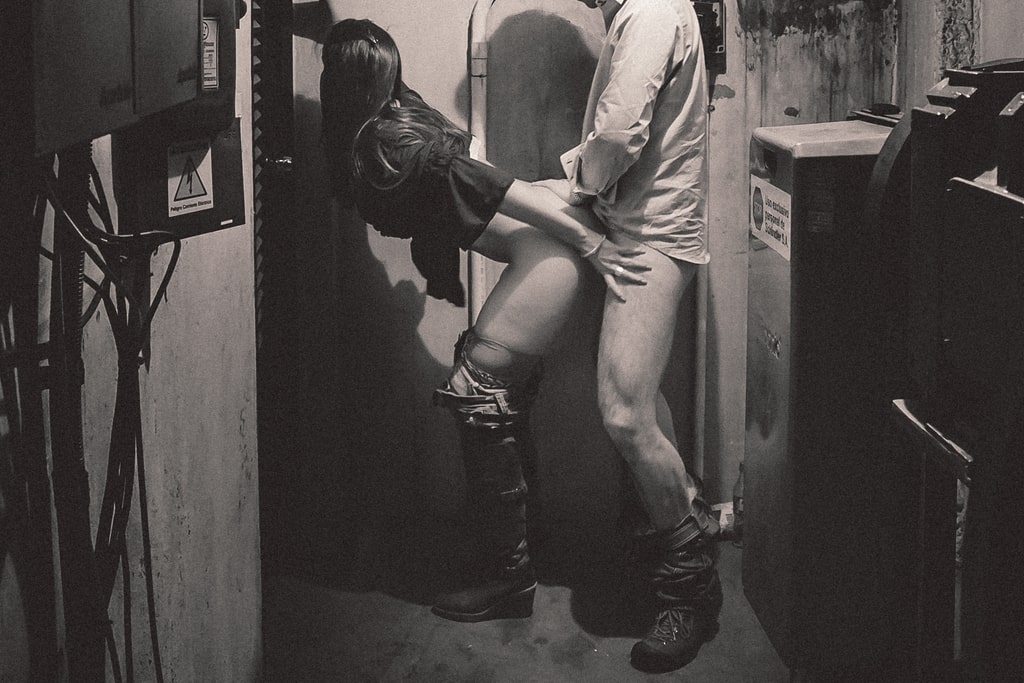 couple with their pants down around their ankles having sex from behind in an engine room