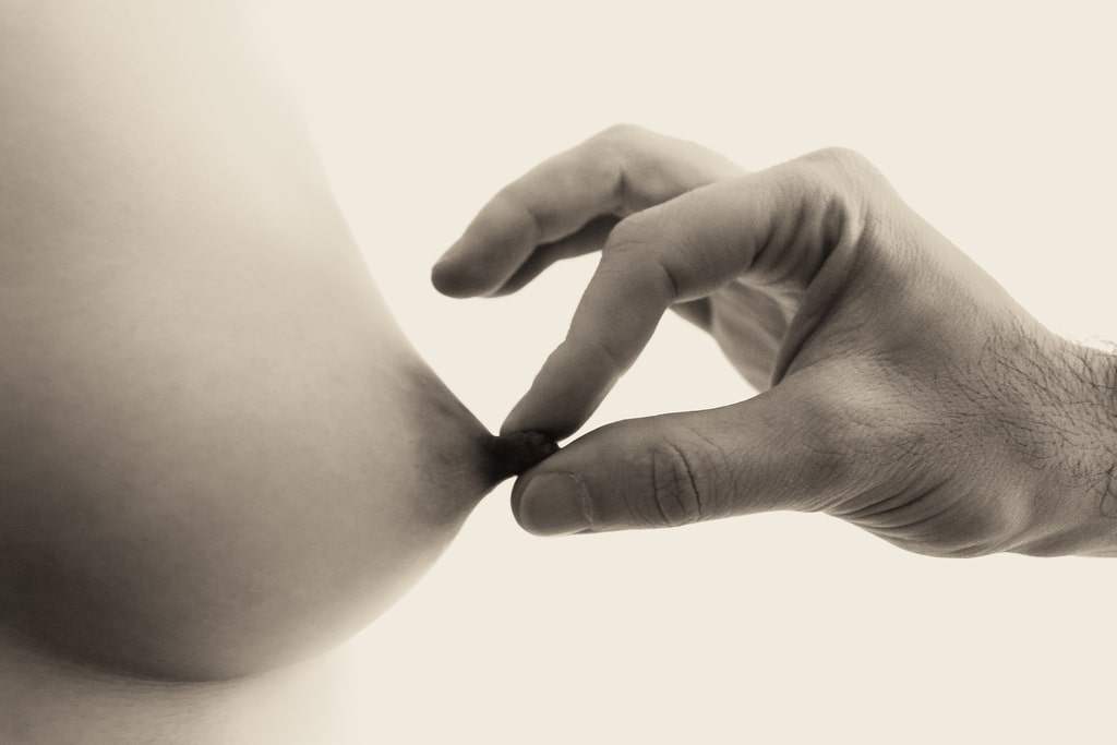 close-up of woman's beckoning breast, her erect nipple being pinched by a man's fingers